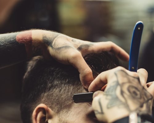 Crop stylish applying foam on customer's cheeks for shaving while working in barbershop.