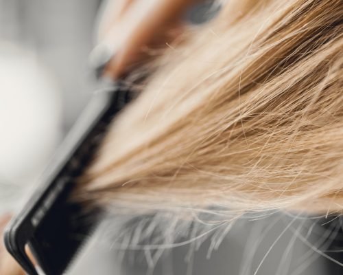 Girl combing blonde hair with a brush. Closeup