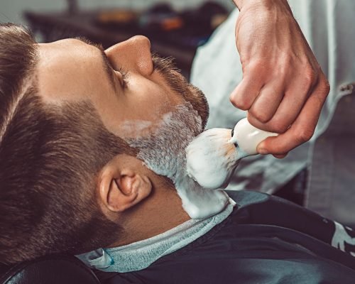 Hipster client visiting barber shop. The hands of young barber making the cut of beard